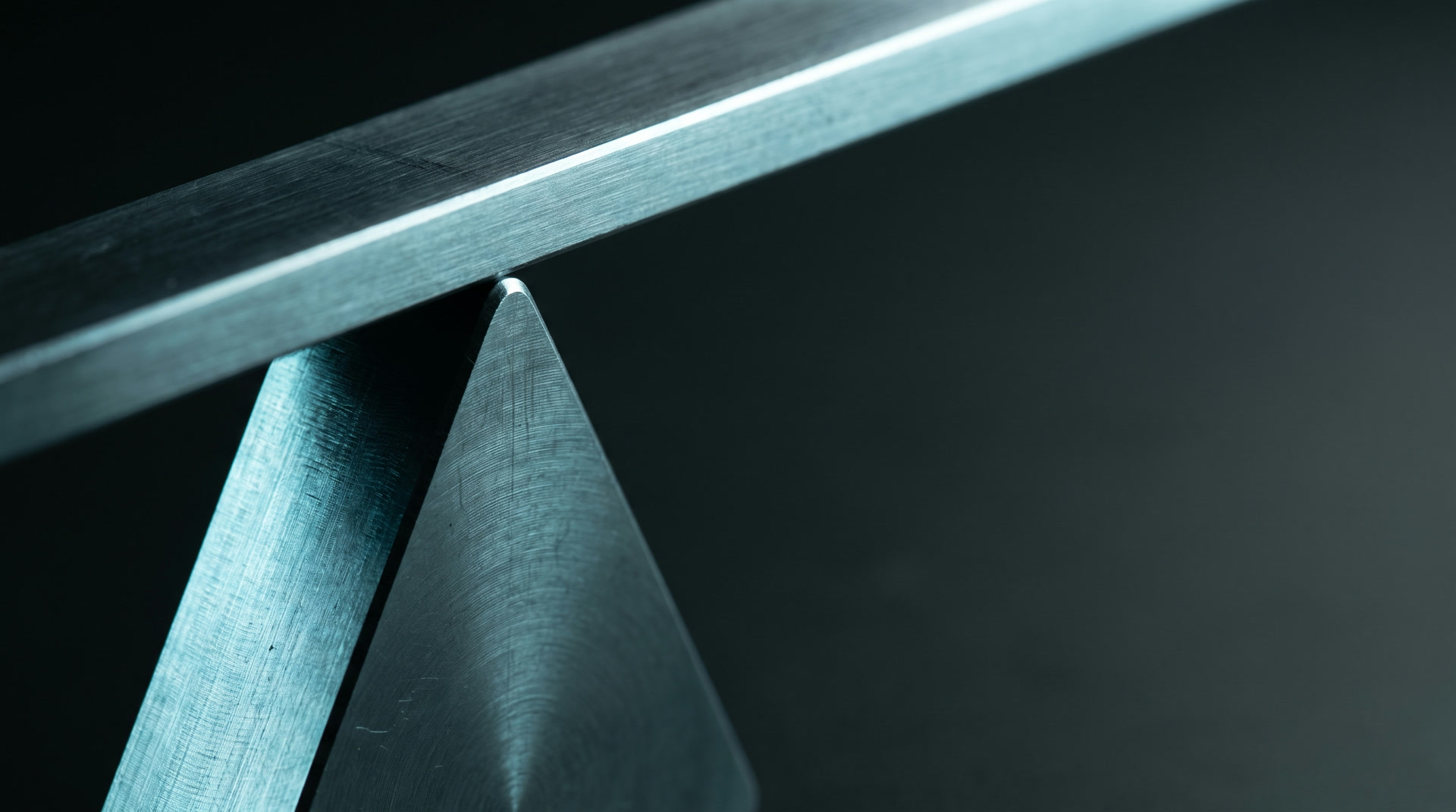 A machined steel beam resting on the point of a triangular pivot.